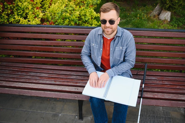 Blind man reading book on bench in park