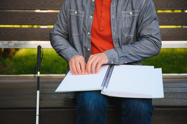 Blind man reading book on bench in park