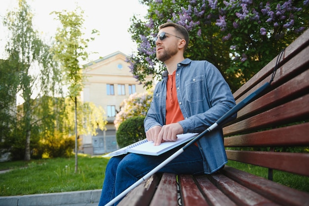 Blind man reading braille book sitting on bench in summer park resting