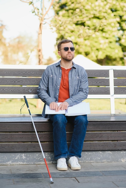 写真 休んでいる夏の公園のベンチに座って点字の本を読んで盲目の男