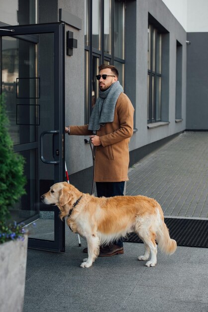 Photo blind man with guide dog and walking stick opening door of building