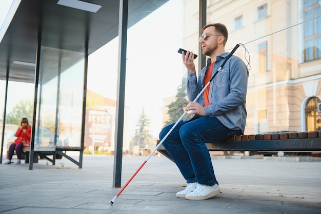 Blind man with white cane waiting for public transport in city