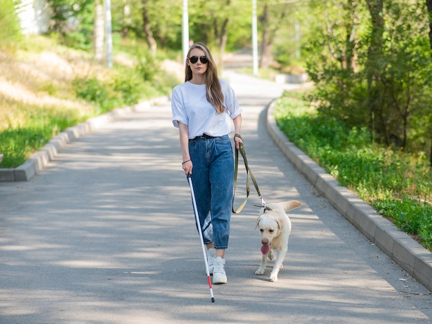 公園で盲目の女性がガイドドッグと歩いています