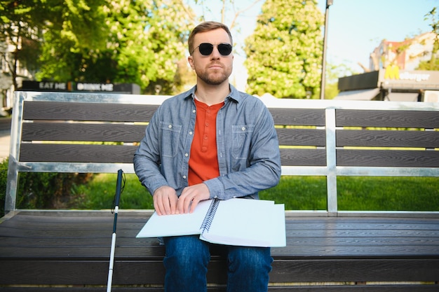 Blinde man leest brailleboek zittend op een bankje in het zomerpark te rusten