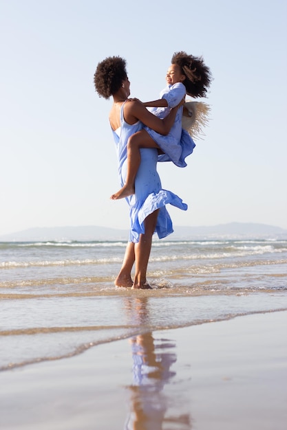 Blissful family having fun on beach. African American mother and daughter making faces, hugging, laughing, fooling around, jumping. Leisure, family time, fun concept