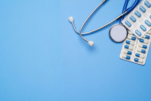 blister of pills capsiles and stethoscope isolated on blue background