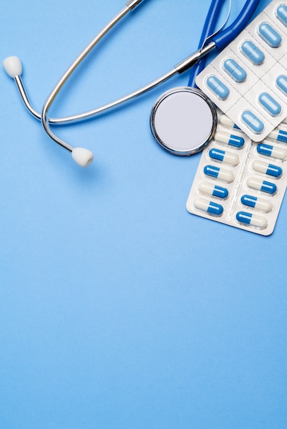 blister of pills capsiles and stethoscope isolated on blue background