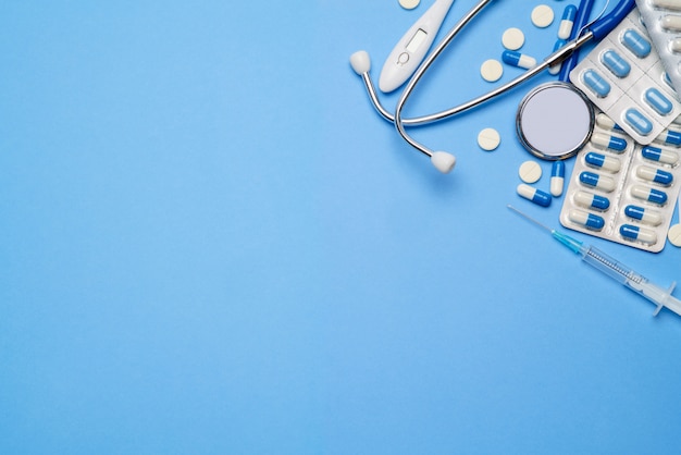 Photo blister of pills capsiles, thermometer, syringe and stethoscope isolated on blue background