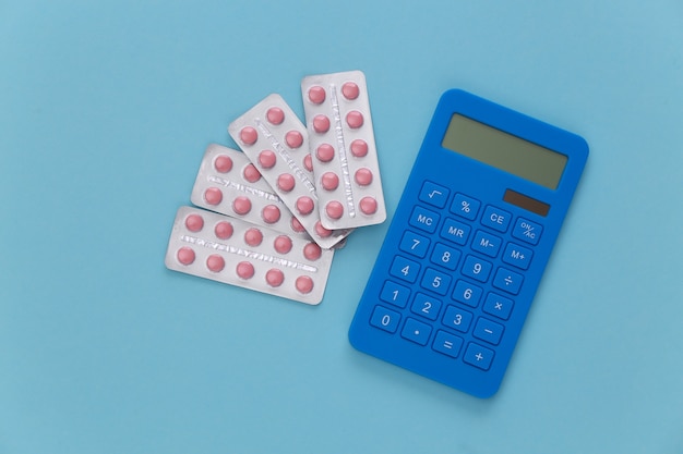 Blisters of pills and calculator on a blue background. Top view