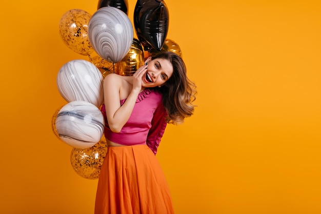 Blithesome birthday girl posing with smile Lovable lady standing on yellow background with party balloons