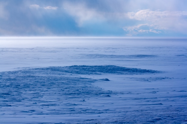 Blizzard op het Baikalmeer in de winter. Harde wind en veel sneeuw. Blauwe schaduw van sneeuw. Wolken in de lucht. Horizontaal.