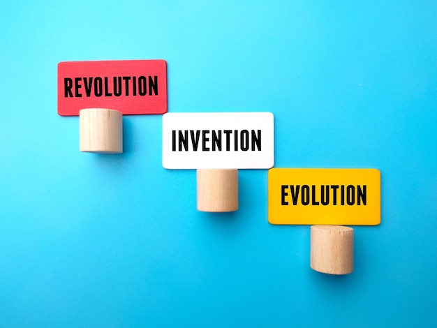 Block cylinder and colored wooden cube with word REVOLUTION INVENTION EVOLUTION on blue background