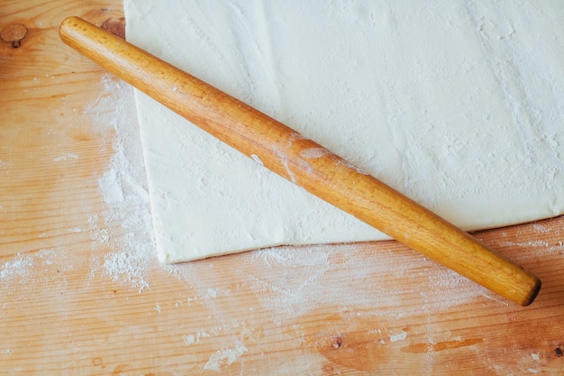 Block of freshly made pastry rolled out on a floured work surface with a wooden rolling pin