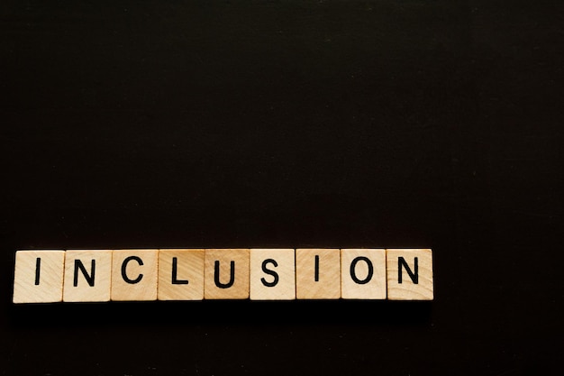 Photo a blocks of wood with the word inclusion on it on a black background