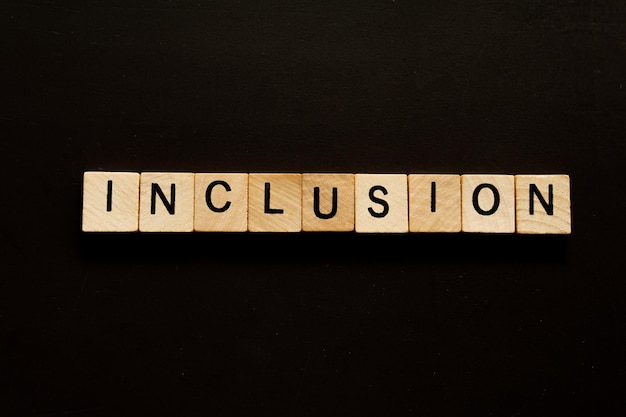 Photo a blocks of wood with the word inclusion on it on a black background