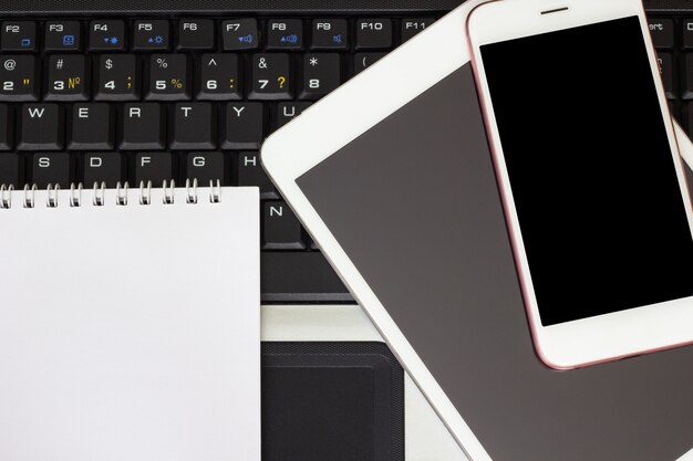 Blocnote, smartphone en tablet op het laptop toetsenbord, bedrijfsconcept