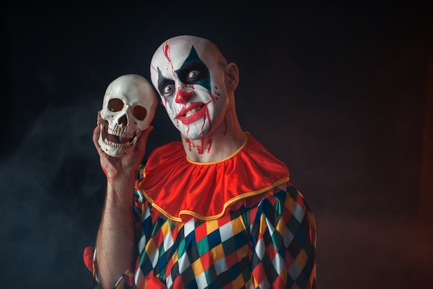 Bloedige clown met gek gezicht houdt menselijke schedel vast