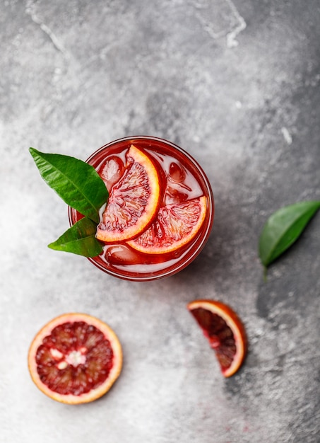 Foto bloedsinaasappelsap met ijs en sinaasappelplak. frisse zomer cocktail met rode sinaasappels in een glas.