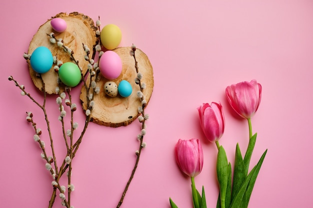 Bloeiende wilgentak, tulpen en paaseieren op houten onderzetters, roze achtergrond