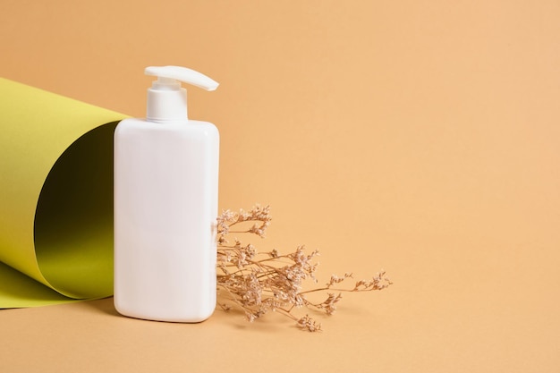 Foto bloem en mock-up lege witte fles met dispenser voor cosmetica op de achtergrond van een rol groenboektextuur, concept van natuurlijke cosmetica