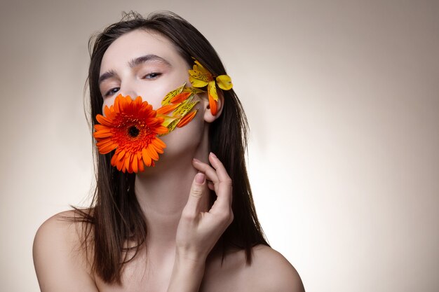 Bloem in mond. Aantrekkelijk teder model met natuurlijke uitstraling met oranje bloem in haar mond