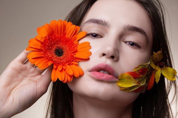 Bloemblaadjes en gezicht. Aantrekkelijk donkerharig model zonder make-up poseert met bloemblaadjes op het gezicht