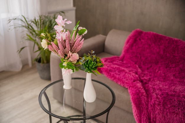 Bloemboeket met prachtige oranje, paarse bloemen kunstmatige en sappige cactus op glazen tafel en palmboom en sofa in de muur. woonkamer interieur.