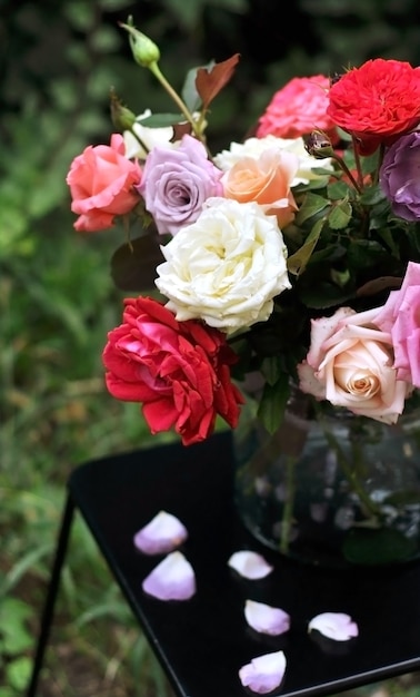 Bloemen boeket van verschillende multi gekleurde rozen in een glazen vaas op een donkere tafel met gevallen bloemblaadjes. Lente zomer boeket