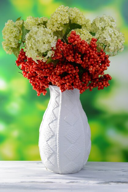 Bloemen en bessen in vaas, op houten tafel, op lichte achtergrond