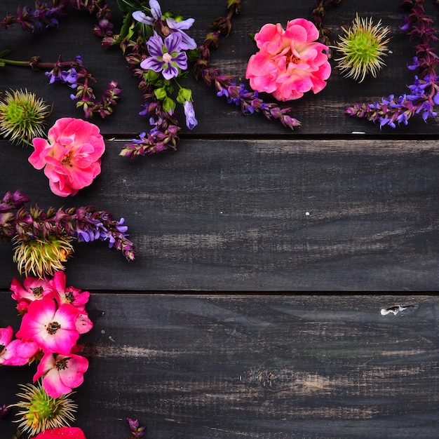 Bloemen in een halve cirkel op een houten achtergrond Briefkaart voor de vakantie Rozen lavendel salie en harige kastanjes langs de randen op donkere planken Achtergrond kopie ruimte plat lag Feestelijke poster