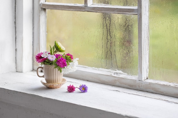 Bloemen in kopje op oude witte vensterbank