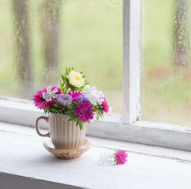 Bloemen in kopje op oude witte vensterbank