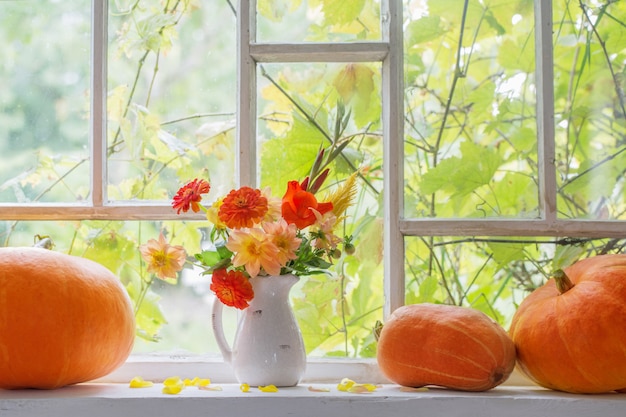 Bloemen in vaas en pompoenen op vensterbank