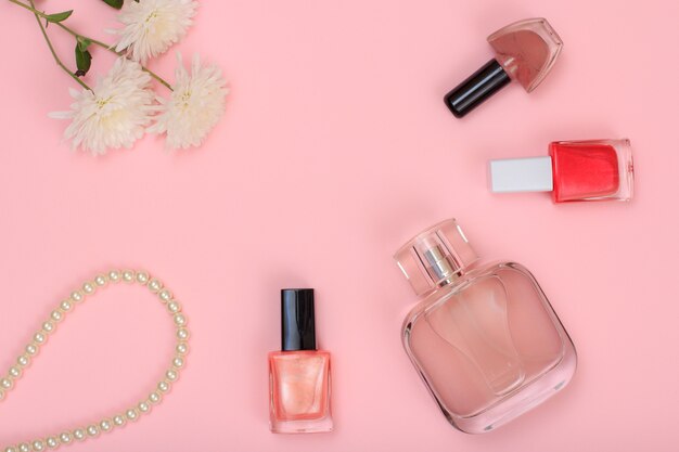 Bloemen, kralen, flesje parfum en flessen met nagellak op een roze achtergrond. Vrouwen cosmetica en accessoires. Bovenaanzicht.