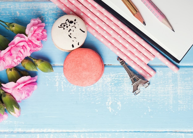 Bloemen, macarons, papieren rietjes, potloden en souvenir Eiffeltoren op de blauwe tafel, bovenaanzicht