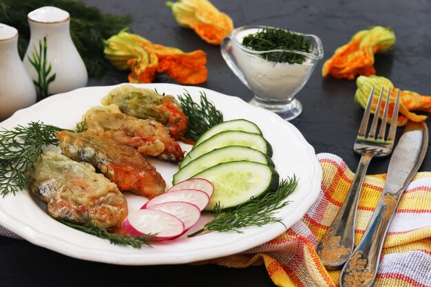 Bloemen van courgette, gekookt in beslag, plakjes komkommer en radijs op een bord