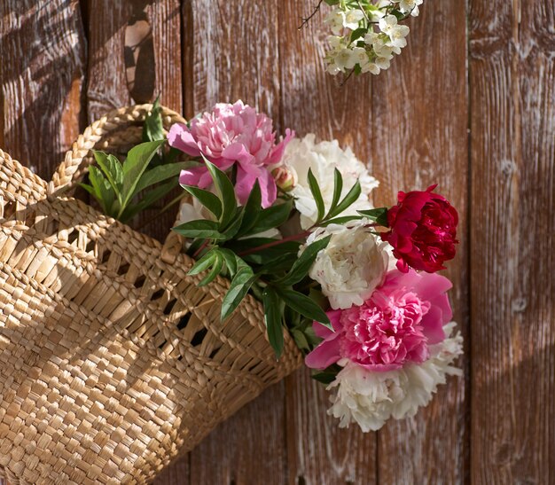 Bloemen van roze rode en witte pioenrozen in rieten mand op houten tafel tegen houten achtergrond