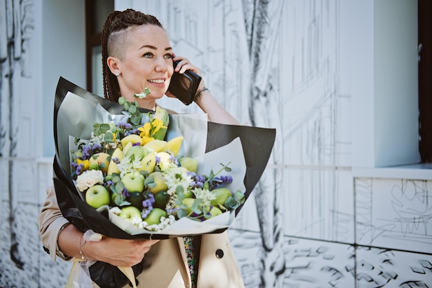 Bloemenbezorging jonge moderne hipstervrouw met mobiele telefoon die een prachtig bloemenboeket ontvangt van