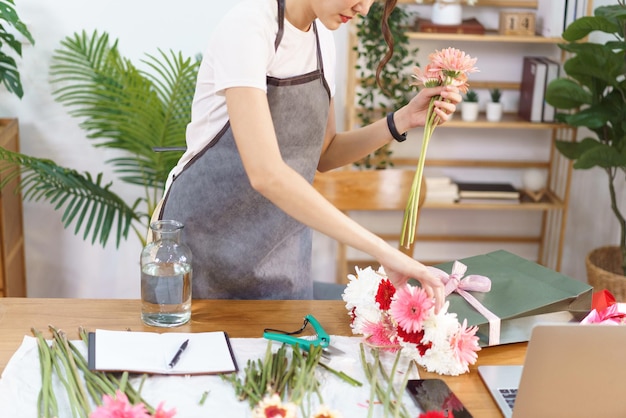 Bloemenwinkelconcept Vrouwelijke bloemist pakt kleurrijke gerbera in boodschappentas om in vaas te schikken