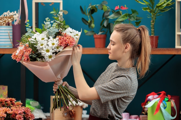 Bloemist maakt een boeket. een jong volwassen meisje houdt een groot boeket veelkleurige chrysanten in haar handen en controleert het.