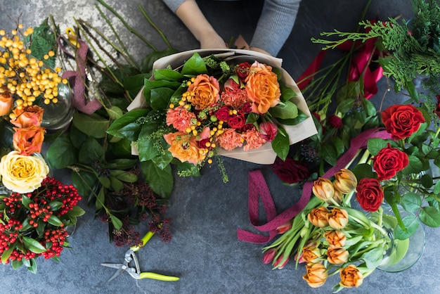 Bloemist maakt een boeket in een bloemenwinkel. Bovenaanzicht van een mooi boeket van rode, oranje, bordeaux, gele rozen, tulpen.