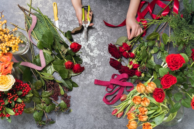 Bloemist maakt een boeket in een bloemenwinkel. Bovenaanzicht van het maken van een boeket van rode, oranje, bordeaux, gele rozen, tulpen.