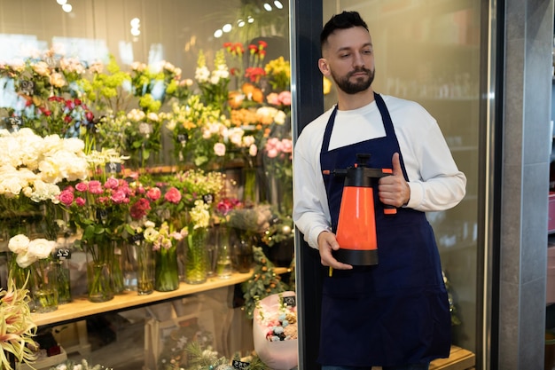 Bloemist met handspuit naast koelkast voor verse bloemen