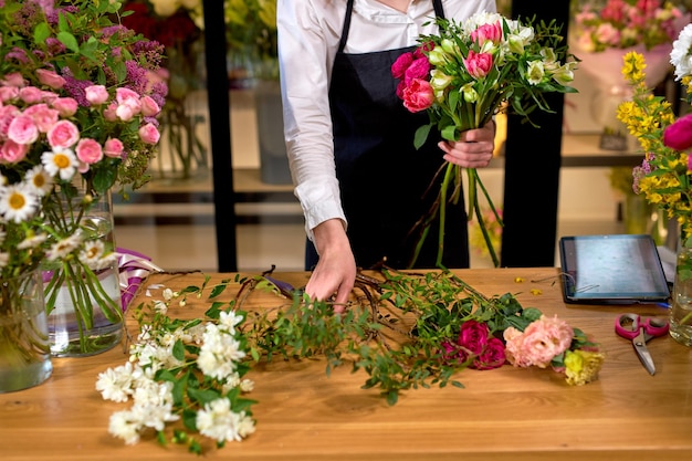 Bloemist op het werk: bijgesneden blanke vrouw die bloemdecoraties schikt, boeket maakt voor klanten. schattige dame in schort staat achter het bureau te werken. bloemisterij, ambacht en handgemaakt concept