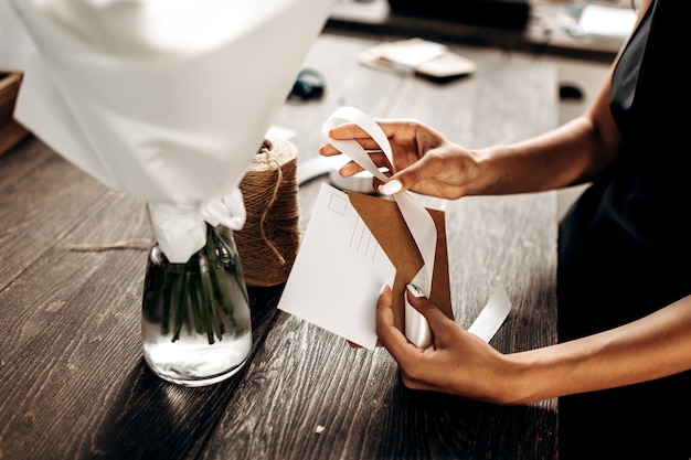 Bloemist pakt een ansichtkaart in een envelop met wit lint op de houten tafel.