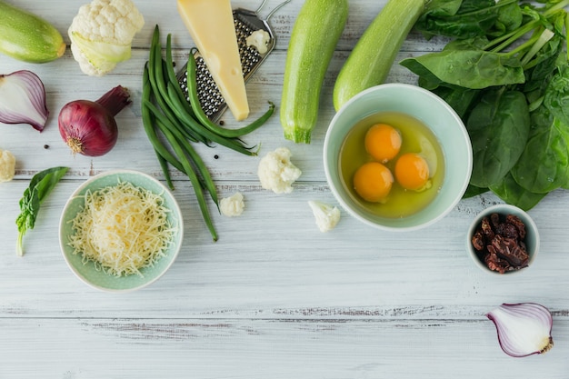 Bloemkool, courgette, rode ui, sperziebonen, eieren, kaas en spinazieblaadjes voor het maken van groentefrittata