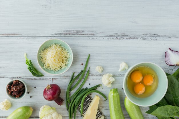 Bloemkool, courgette, rode ui, sperziebonen, eieren, kaas en spinazieblaadjes voor het maken van groentefrittata