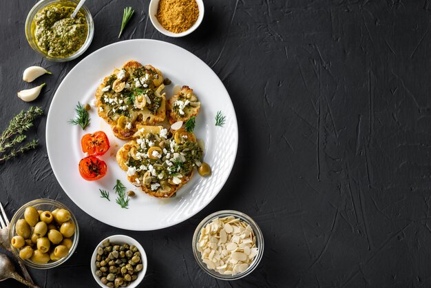 Bloemkool steak met kruiden chimichurri saus amandel vlokken olijven gebakken kerstomaatjes en kappertjes op een witte plaat Vegetarisch eten