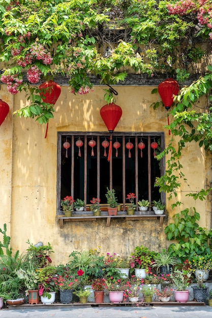 Bloempotten met bloemen, gele muur en raam met rode Chinese lantaarns