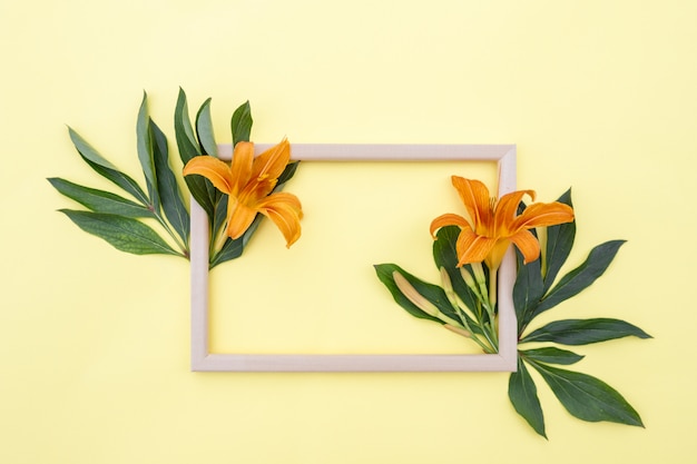 Foto bloemsamenstelling. frame van geeloranje leliebloemen en groene bladeren op een gele achtergrond